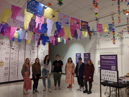 Students in gallery with paper art on walls and ceiling.